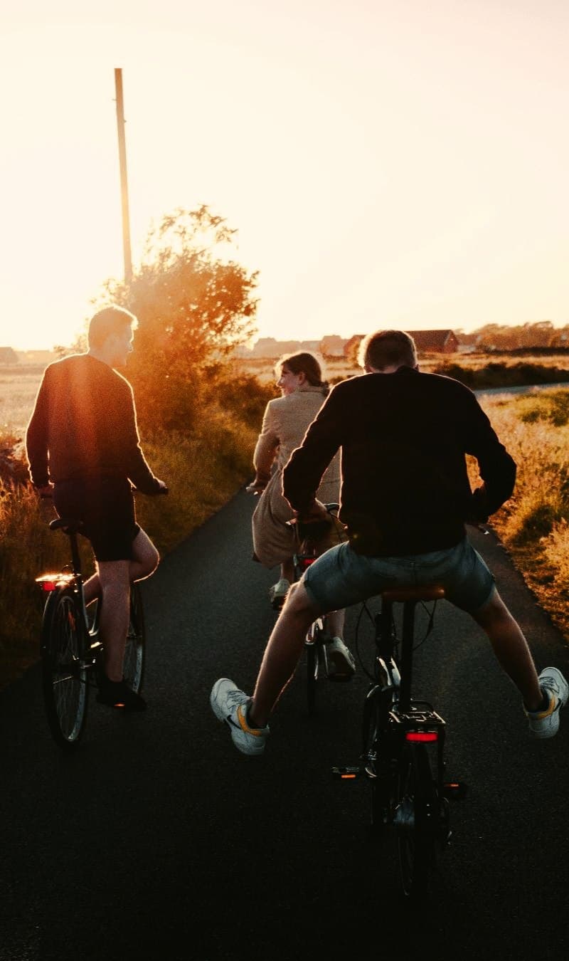 Drie mensen fietsen bij zonsondergang over een fietspad door de polder