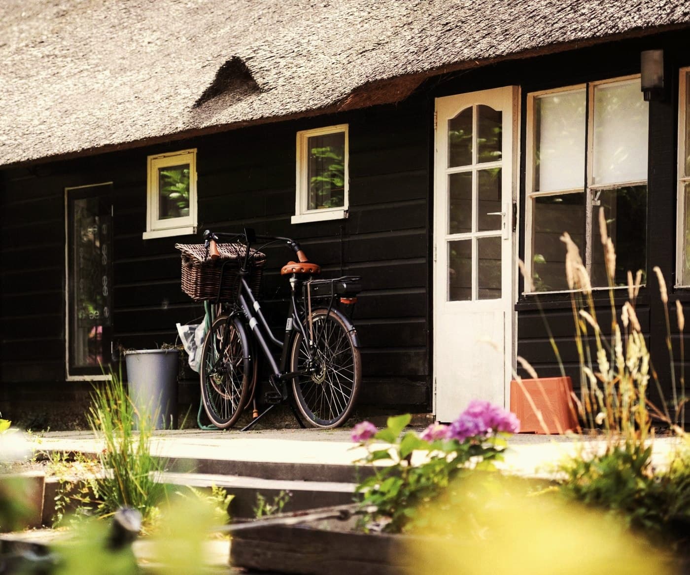 Fiets met mand tegen een rietgedekt houten huisje, naast de witte voordeur